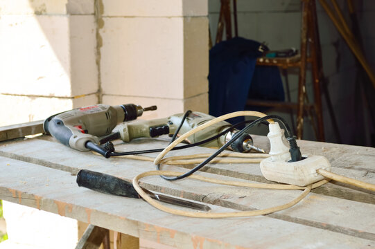 Close-up - A White Extension Cord Lies On A Table Made Of Old Boards Against The Background Of Working Tools And A Construction Site