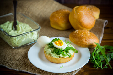 Homemade bun with cheese spread, fresh arugula and boiled egg in a plate