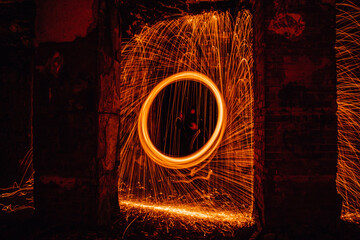 Man spinning glowing steel wool in urban environment producing fire sparkles.