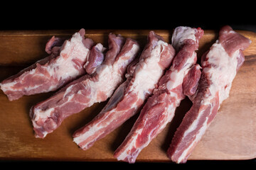 Close-up Raw Pork Ribs on a wooden board on a black background with free space for your text/decoration.