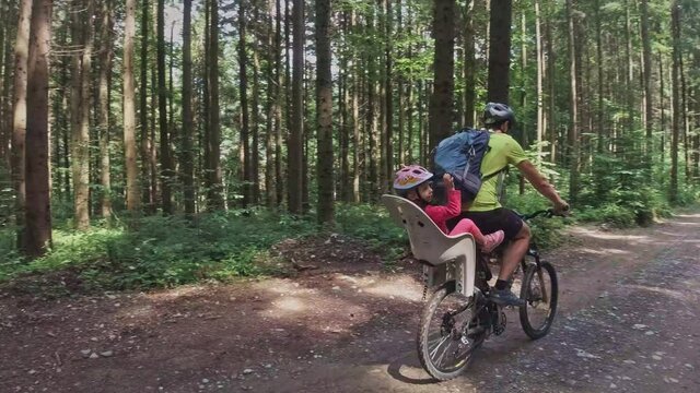 Family time outdoors. Father and little daughter on bike pedaling in the forest