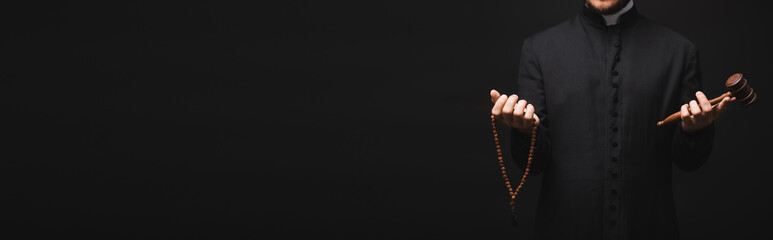 panoramic shot of priest holding wooden gavel and rosary beads in hands isolated on black