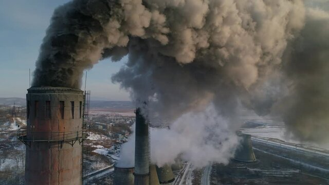 Drone around toxic enterprise chimneys tubing against the sky background release black smoke. Factory pollutes environment. Russia Primorsky Krai industrial countryside landscape. Winter day. Aerial