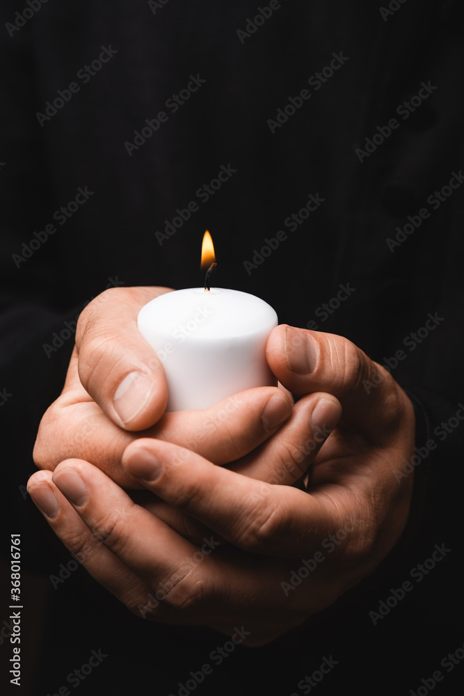 Poster cropped view of priest holding burning candle isolated on black - Posters