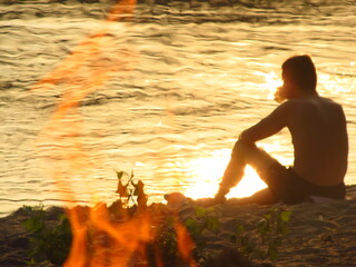 Człowiek siedzący na brzegu rzeki na tle ogniska