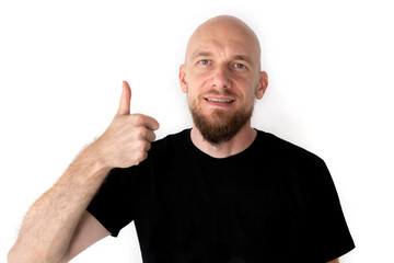 A handsome, strong bald man with a stylish beard shows thumbs up, dressed in black t-shirt, isolated on white background. With copy space for your text.