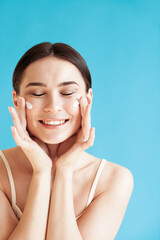 Lovely young woman with healthy skin is applying a cream on her face