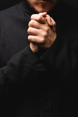 cropped view of priest with clenched hands praying isolated on black