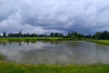 Fototapeta na wymiar Landscape with a fish pond before the rain, dark storm clouds in the background