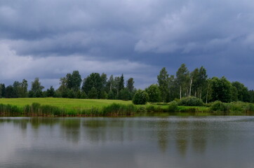 Landscape with a fish pond before the rain, dark storm clouds in the background