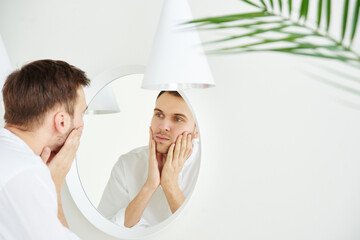 Young attractive Caucasian man examines his face in the mirror close-up. Skin care concept