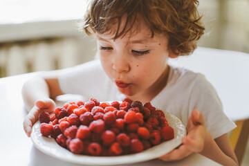 Cute beautiful little boy eating fresh raspberries. Healthy food, childhood and development. Happy kid at home. © Анастасія Стягайло