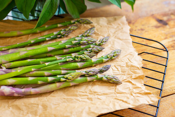 Fresh green asparagus spears wrapped in brown craft paper wrapper for healthy vegetarian cuisine lying on a wooden surface, top view. Close-up.
