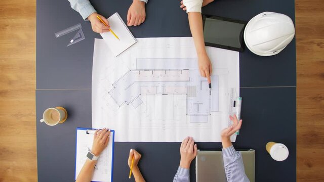 construction business, architecture and team work concept - team of architects with blueprint, gadgets and papers working at office table
