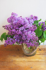 A very beautiful bouquet of purple lilac stands in a vase on a wooden table. Close-up. Spring, warm time.