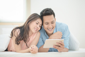 Fototapeta premium Asian couple lovers enjoy watching online movie on smart tablet on holiday vacation in bedroom.