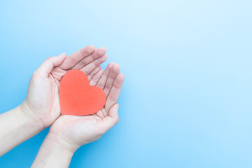 Human hands holding healthy heart shape on light blue background. Concept of organ donation, heart...