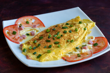 omelet with cooked ham cheese and tomato with green onion in white square plate