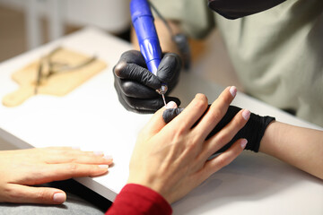 The woman holds the clients hand and processes the cuticle with a special apparatus
