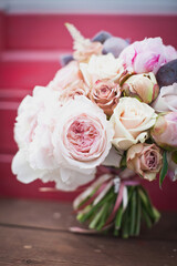 Wedding bridal bouquet of blooming live roses, pink and white peonies. Tied with silk ribbons. Against a bright background.