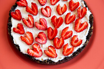 A strawberry cheesecake decorated with a heart-shaped strawberry lies on a coral-colored plate. Illustration of a cheesecake recipe with strawberries.