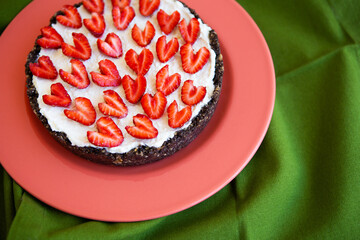 A strawberry cheesecake decorated with heart-shaped strawberries lies on a coral-colored plate and stands on a green napkin. Illustration of a cheesecake recipe with strawberries. Close-up.