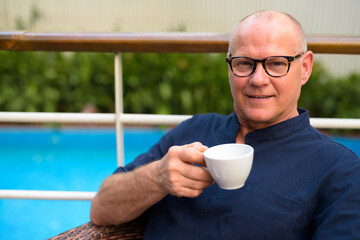 Happy senior handsome tourist man drinking coffee and relaxing with nature outdoors