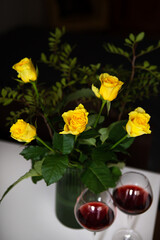 Obraz na płótnie Canvas A very beautiful bouquet of yellow roses stands in a green vase and two glasses of red wine. Romantic evening.