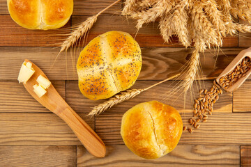 Top view on a rolls with ears, grains and knife with butter on a wooden table