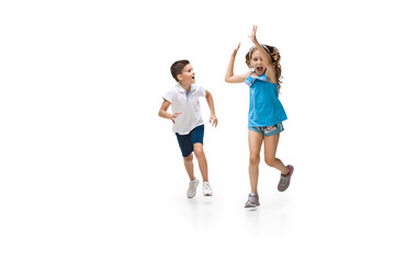 Happy kids, little and emotional caucasian boy and girl jumping and running isolated on white background. Look happy, cheerful, sincere. Copyspace for ad. Childhood, education, happiness concept.