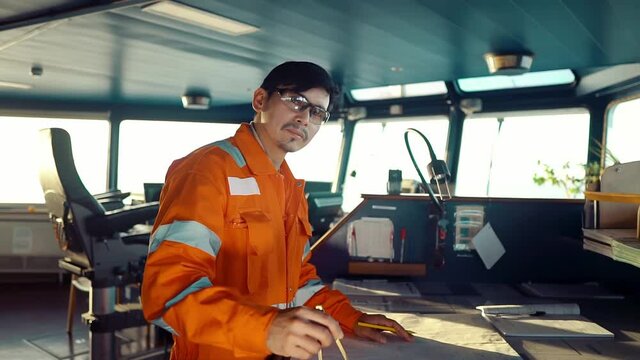 Filipino deck Officer on bridge of vessel or ship wearing coverall during navigaton watch at sea