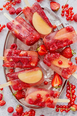 Homemade raspberry, strawberry, apple and currant popsicles on metal plate with ice assorted berries