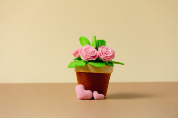 The pot of handmade felt roses on a beige background with pink hearts. Copy space. Child gift concept, holiday card, congratulation, invitation.