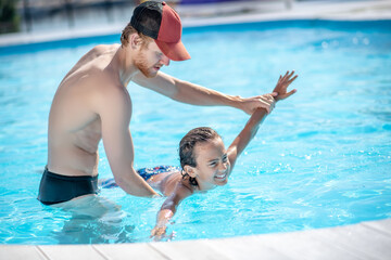 Bearded man teaching boy to swim in pool