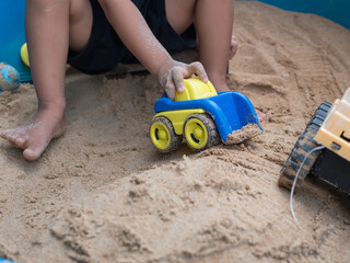 Hand of child boy playing car toy in sandbox outdoor. Happy kid enjoy in relaxing day.