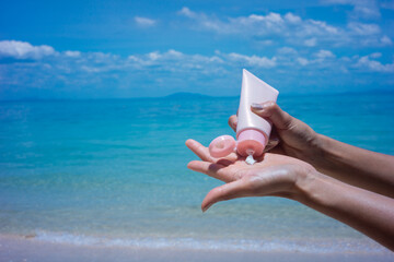Woman applying sunscreen on her hands from a bottle on the beach with the sea in the background. SPF sunblock protection concept.selective focus