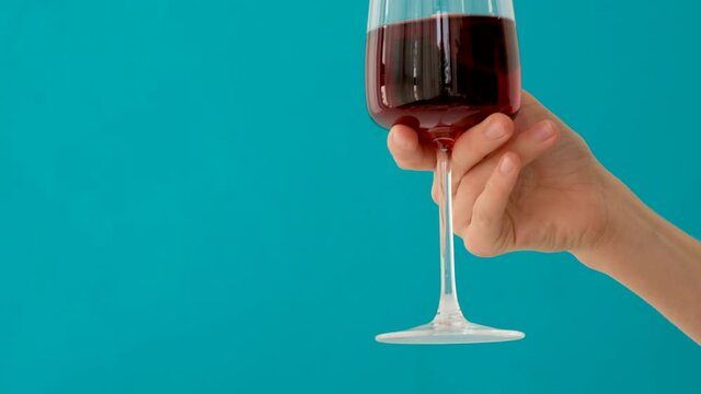 Hand holding wine red wine glass against blue backround
