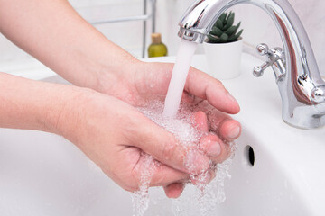 Man washing his hands, close-up hands of man at bathroom with soap and flow of water, concept...