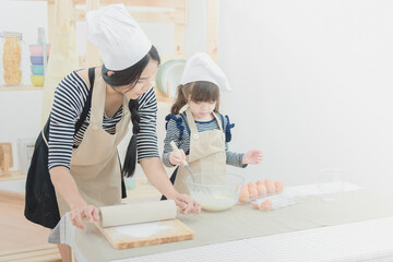 Obraz na płótnie Canvas Happy family in the kitchen of Asian mother and her daughter preparing the dough to make a cake.