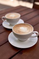 Two cups of cappuccino on the wooden background. Beautiful brown foam, white ceramic cups, place for text