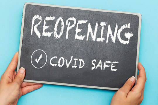 hands holding chalkboard with notice reopening covid safe