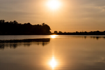 Fototapeta na wymiar Scenic view of Sunset above the lake. Sun reflecting out of water surface. Landscape photo