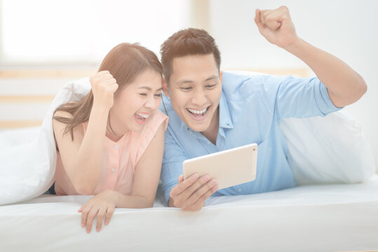 Happy Family,Asian couple lovers enjoy cheer up  and watching football sport live streaming on smart tablet.Photo series of family and happy people concept.