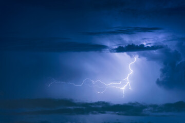Thunder storm lightning strike on the dark cloudy sky background at night.