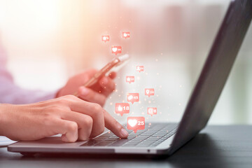 Businessman using laptop computer and mobile phone to play social media icon such as love like and...