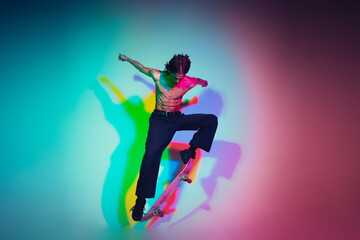 Fototapeta na wymiar Skateboarder doing a trick isolated on studio background in colorful neon light. Young man shirtless riding and skateboarding in motion. Concept of leisure activity, sport, extreme, hobby and motion.