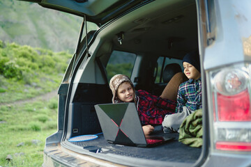 two boys watching a video on a laptop in the trunk of a car