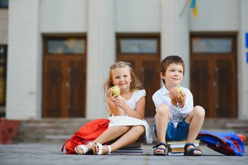 Fototapeta premium Two pupils of primary school. Boy and girl with school bags behind the back. Beginning of school lessons. Warm day of fall. Back to school. Little first graders.
