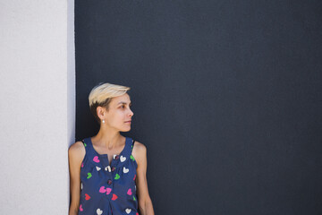 A girl with short hair stands against a dark gray wall