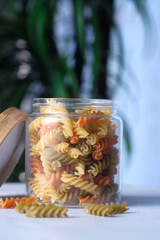 colorful uncooked macaroni in jar on table .